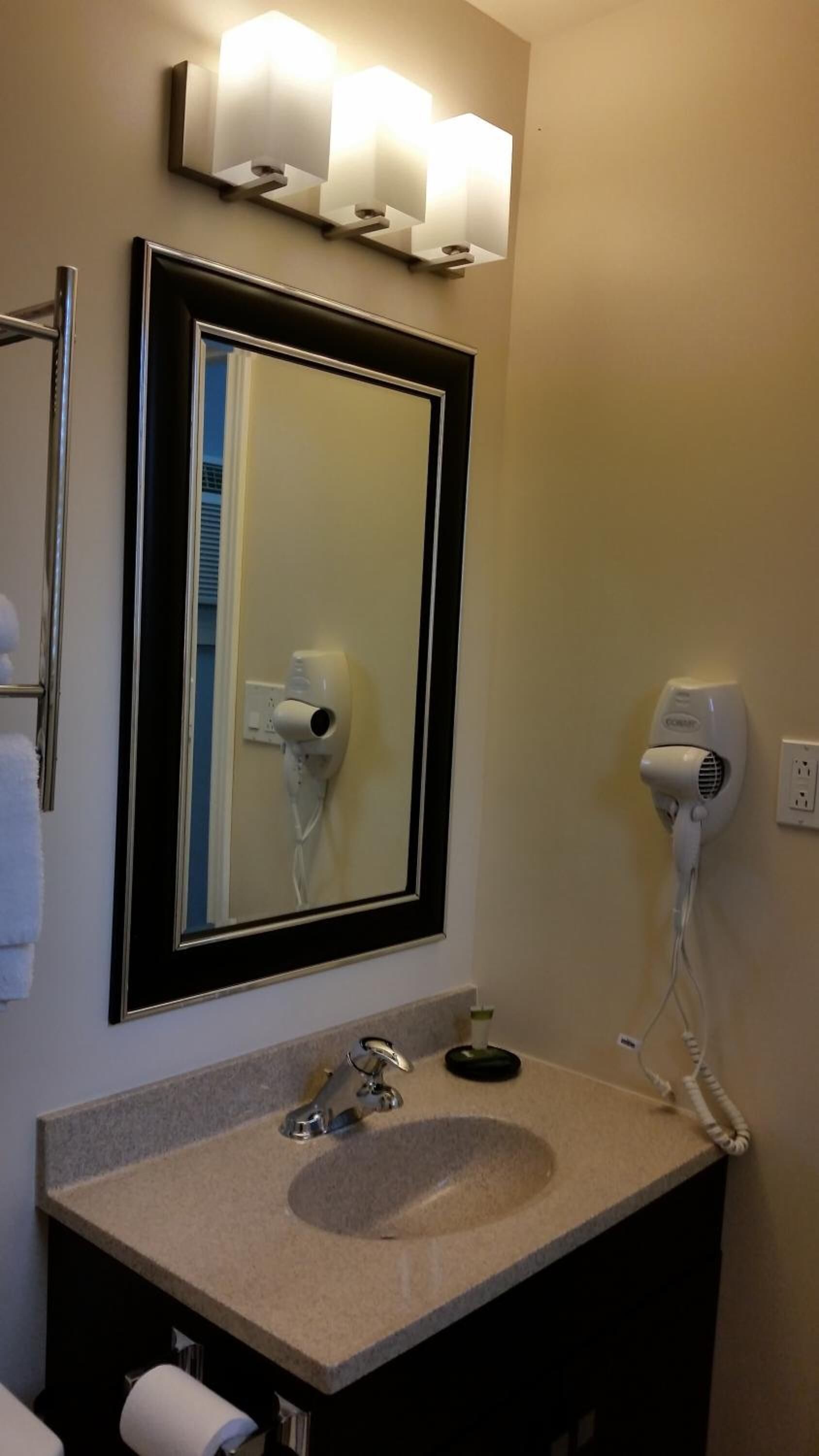 Une salle de bain équipée d’un lavabo, d’un miroir, d’un sèche-cheveux et d’un porte-serviettes.