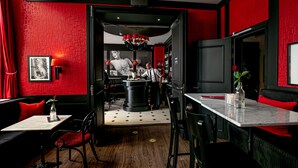 A modern bar with red and black decor, featuring a bar counter, stools, and a large chandelier. - Le Theatre Hotel (Maastricht)