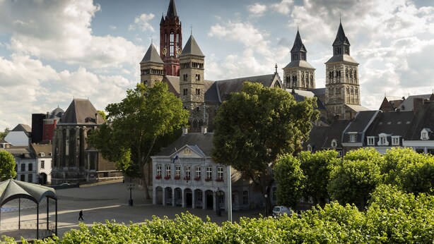 A historic building with multiple towers and a central clock tower, surrounded by trees and other buildings. - Le Theatre Hotel (Maastricht)