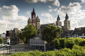 A historic building with multiple towers and a central clock tower, surrounded by trees and other buildings. - Le Theatre Hotel (Maastricht)