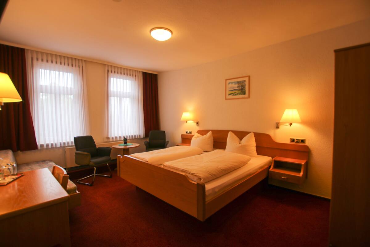 Una habitación de hotel con una cama, dos sillas, un escritorio y una mesita de noche.