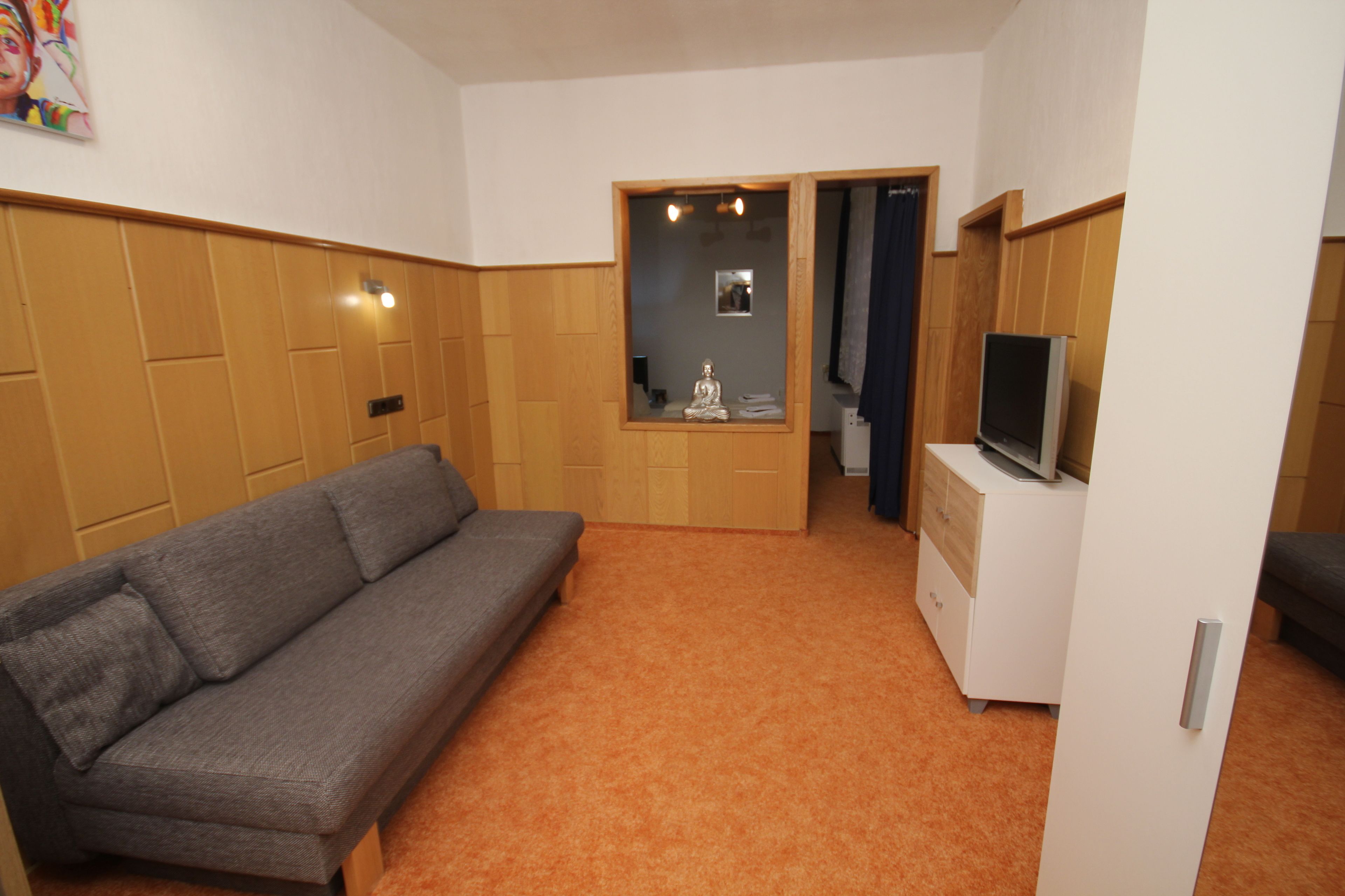 Una habitación con un sofá gris, un mueble bajo con televisor y un espejo con marco de fotos.