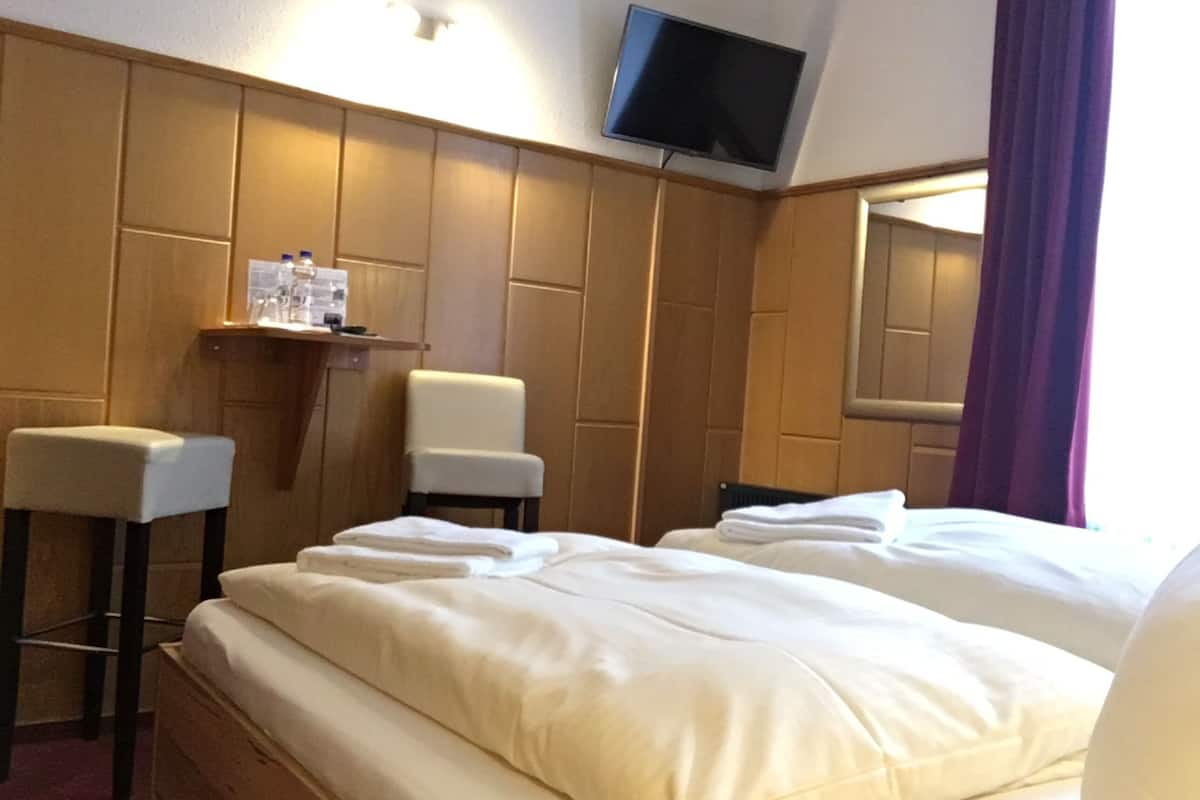 Habitación de hotel con una cama grande, dos sillones, un televisor montado en la pared y una mesita con artículos de aseo.