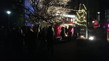 A nighttime outdoor gathering with people around a central fire, illuminated by street lamps and decorated trees.