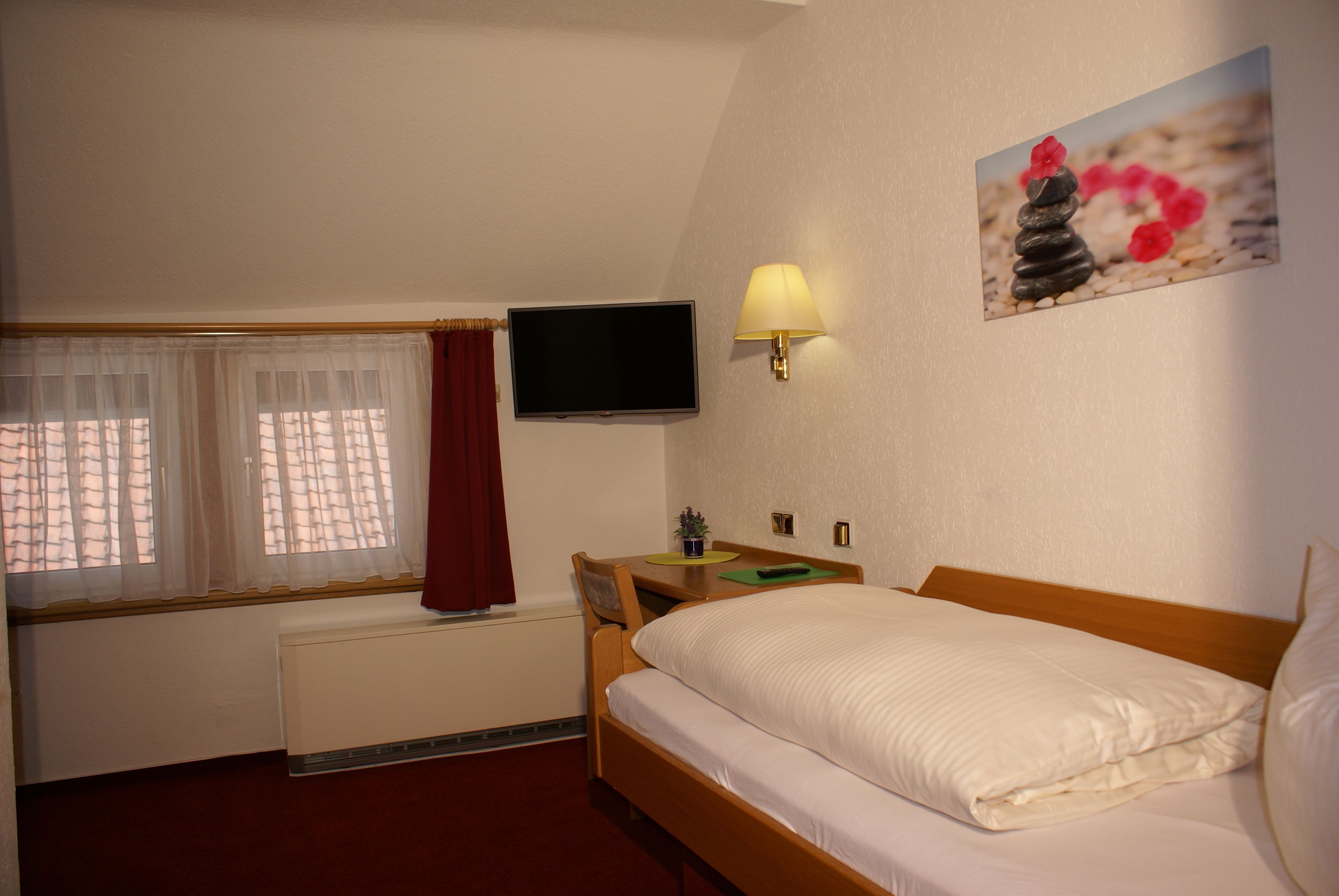 Una habitación de hotel con una cama, televisión, lámpara, ventana con cortinas y un cuadro en la pared.