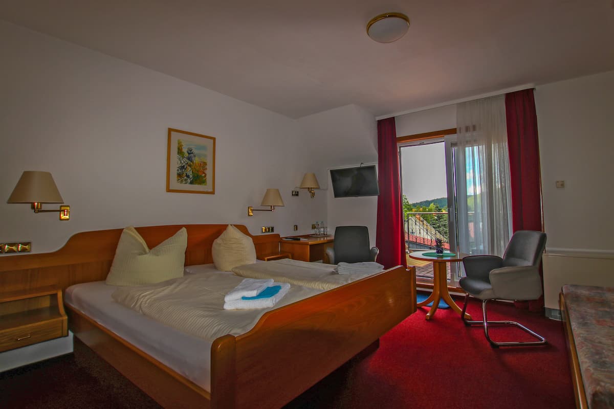 Una habitación de hotel con cama, escritorio, silla, televisión y ventana con cortinas.