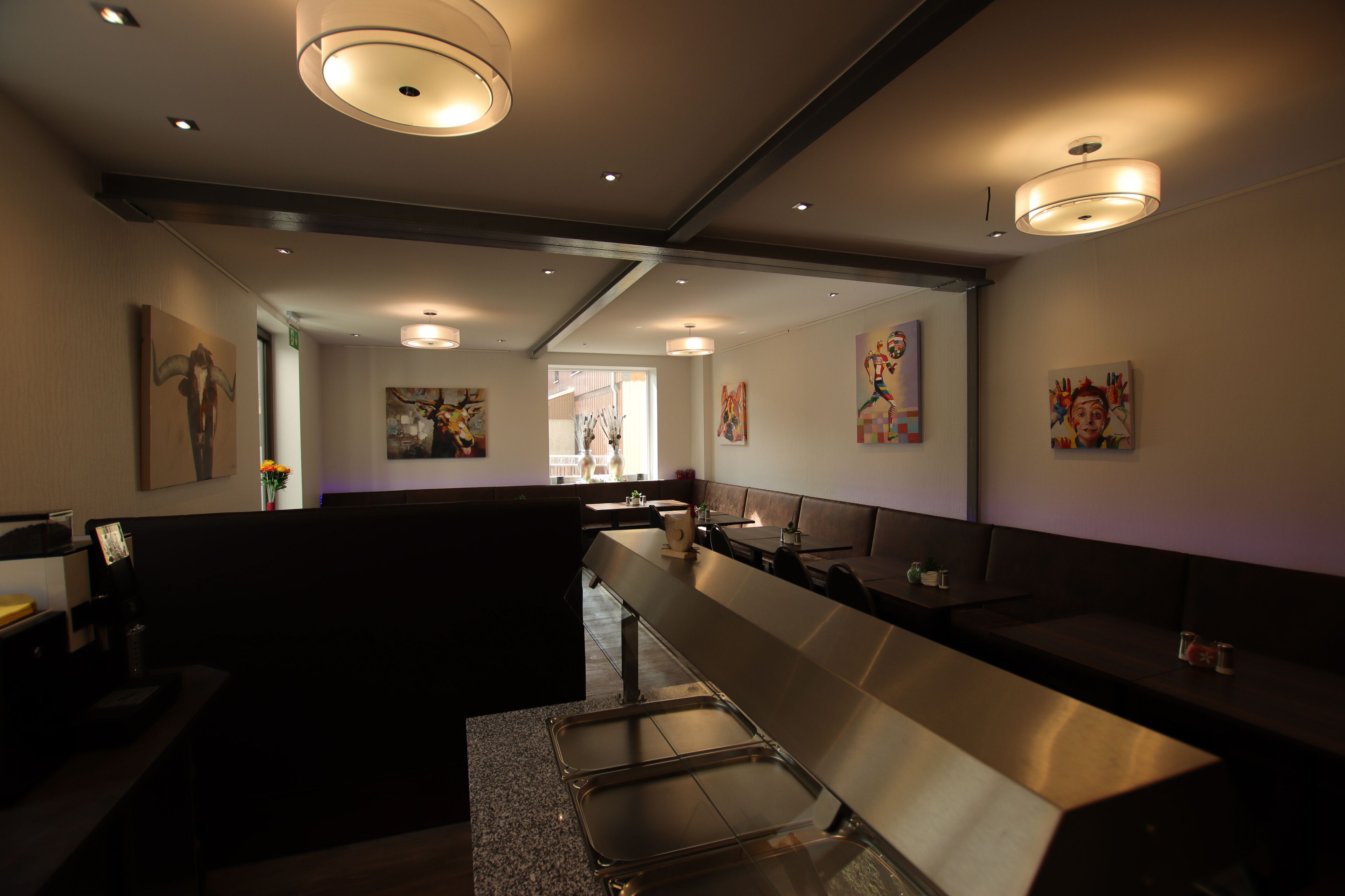 A modern restaurant with a long counter, recessed lighting, and artwork on the walls.