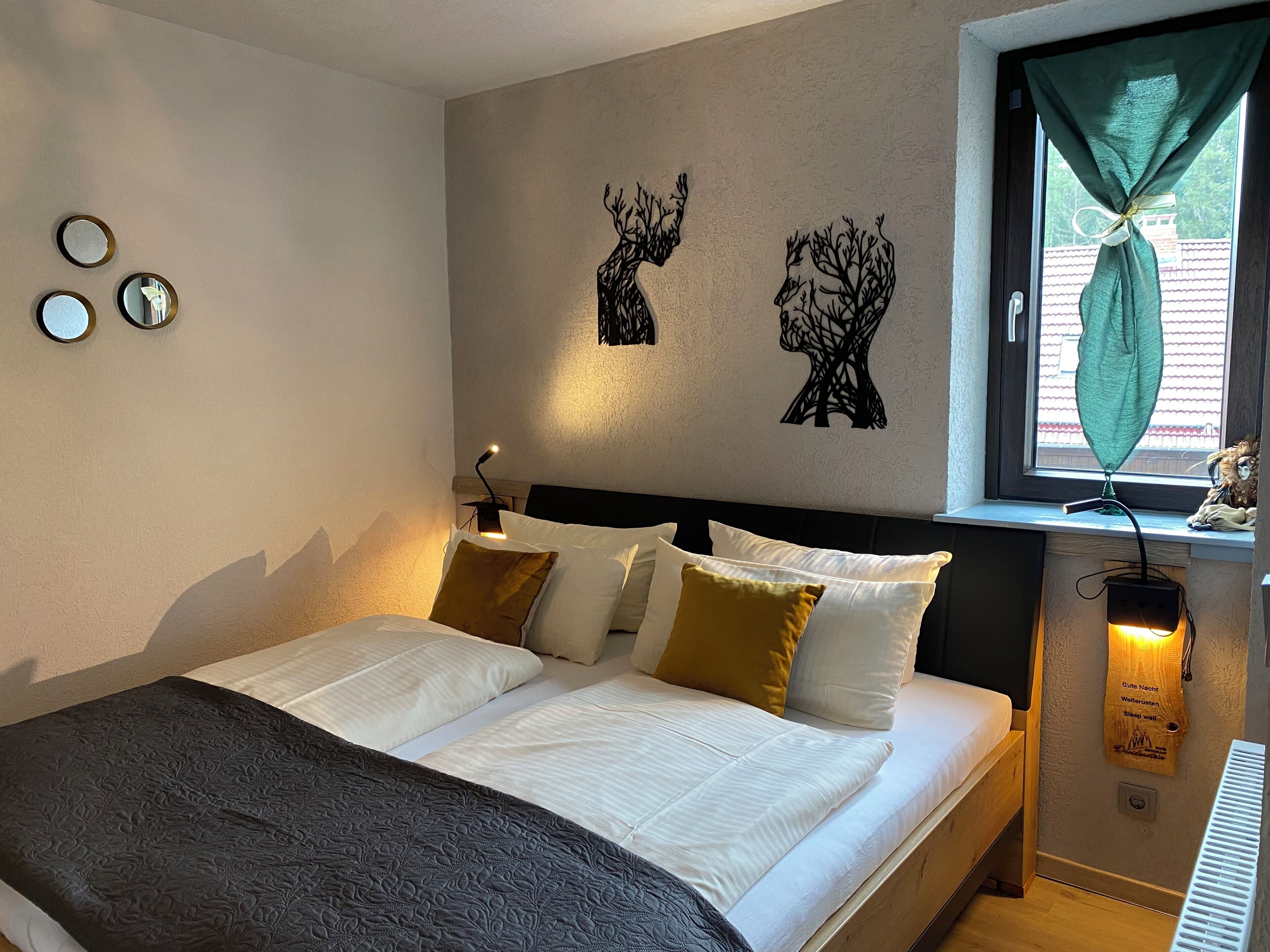 A neatly made bed with white linens and multiple pillows, a wall-mounted lamp, and a window with a curtain.