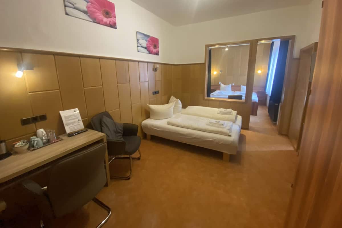 Habitación de hotel con cama, escritorio, silla, espejo y dos cuadros de flores en la pared.