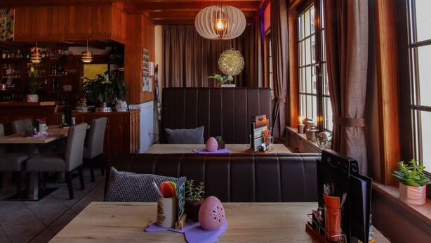 A cozy restaurant with wooden ceilings, a central table, and a bar area in the background. - Hotel-Restaurant Druidenstein (Oberharz am Brocken)