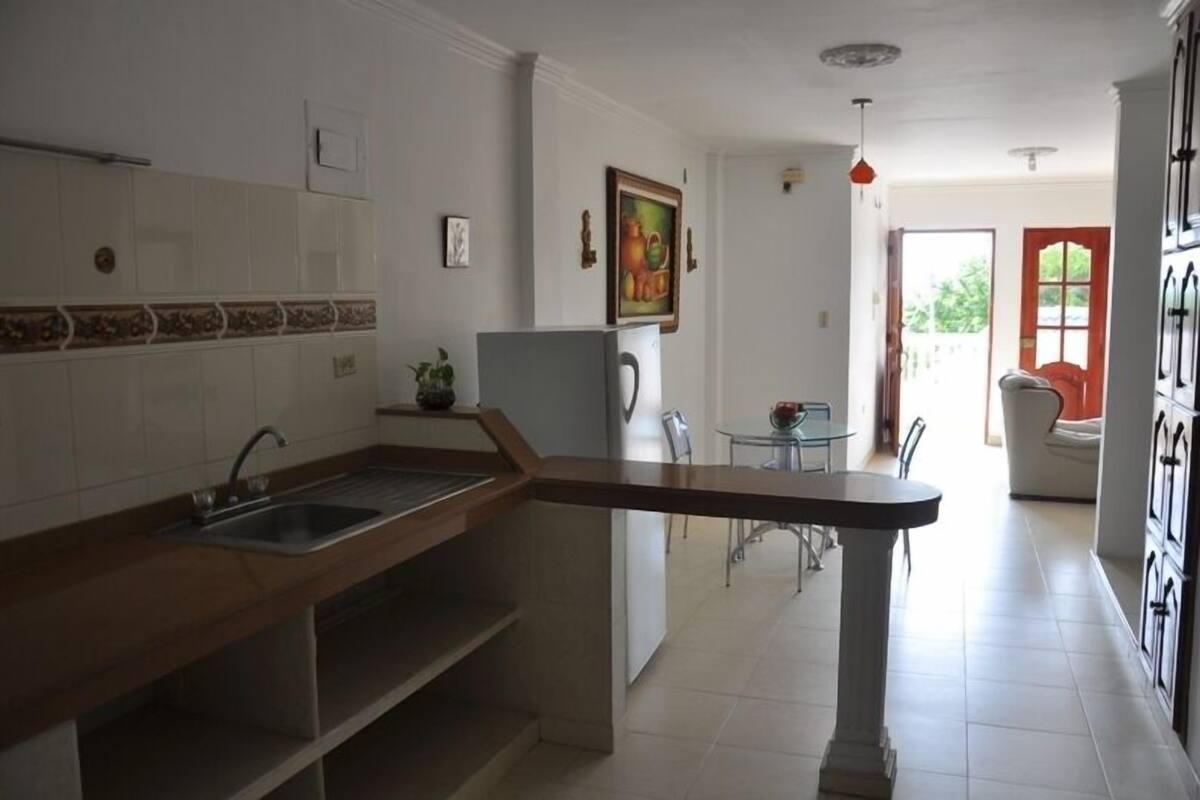 Une cuisine avec un plan de travail en bois, un évier et un réfrigérateur. On y trouve également un coin repas avec une table et des chaises.