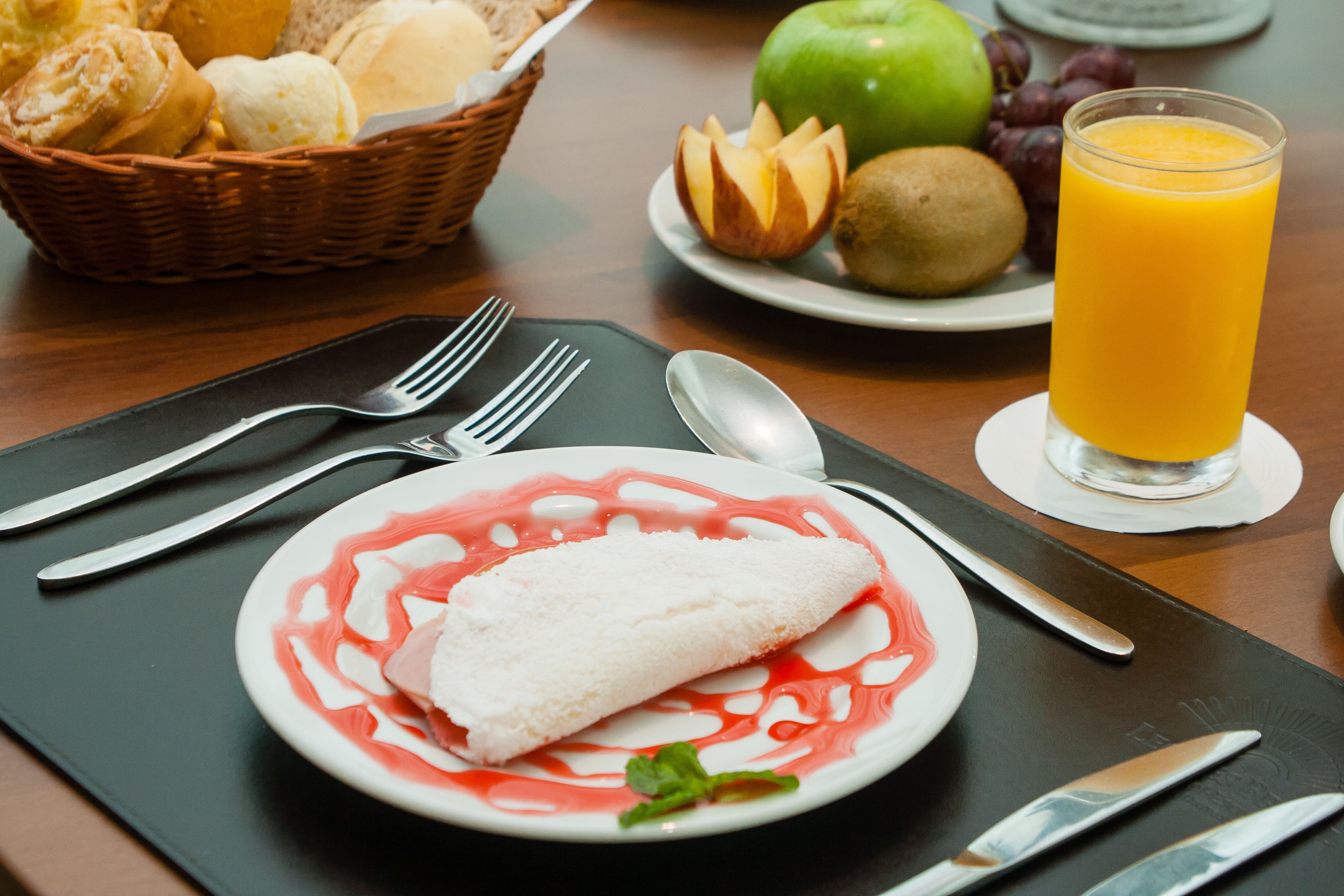A breakfast setting with a plate of food, a glass of orange juice, and a basket of bread.
