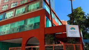 A modern hotel building with a red facade, large windows, and palm trees.