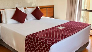 A hotel room with a large bed, white bedding, and a red patterned throw. There are two framed pictures on the wall above the bed.