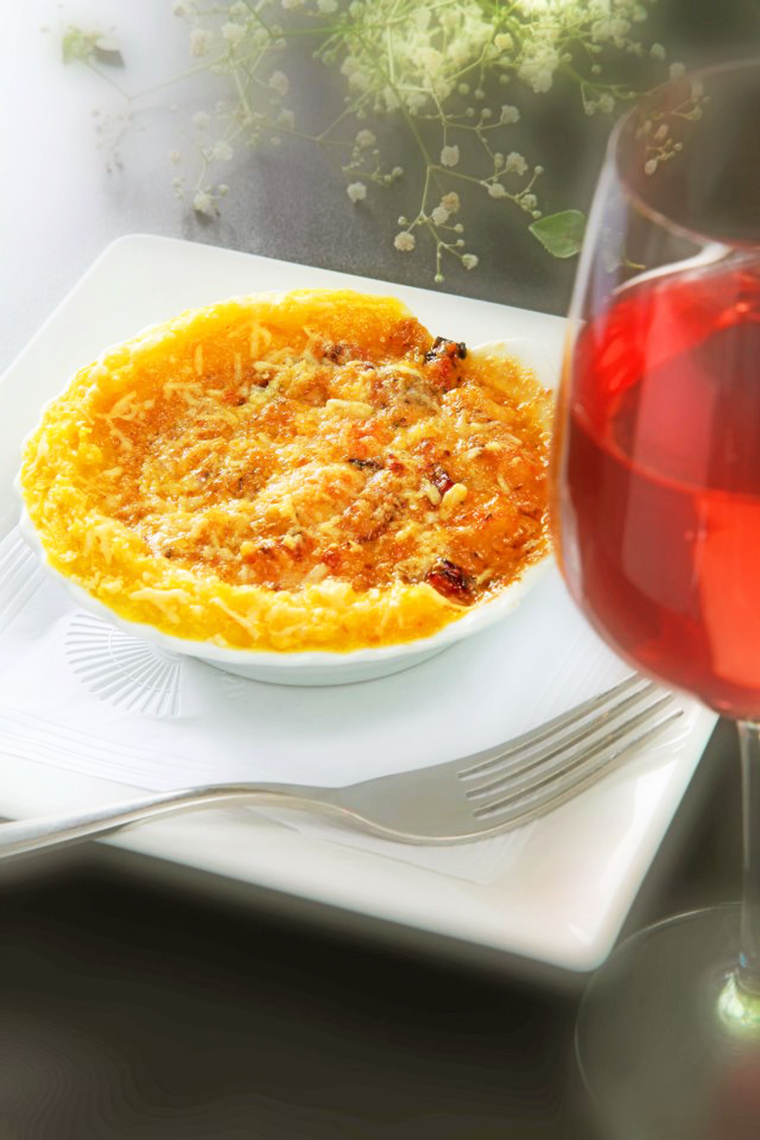 Une assiette blanche contenant un plat cuit au four, un verre de vin rouge et une fourchette posée sur une serviette blanche.