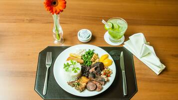 A plate of food with rice, meat, and vegetables, a glass of green drink, a flower in a vase, and a napkin on a wooden table.