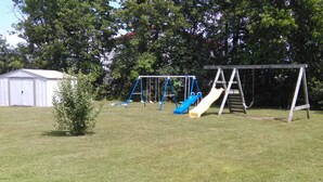 Un parque con césped, un columpio, un tobogán y un cobertizo pequeño.