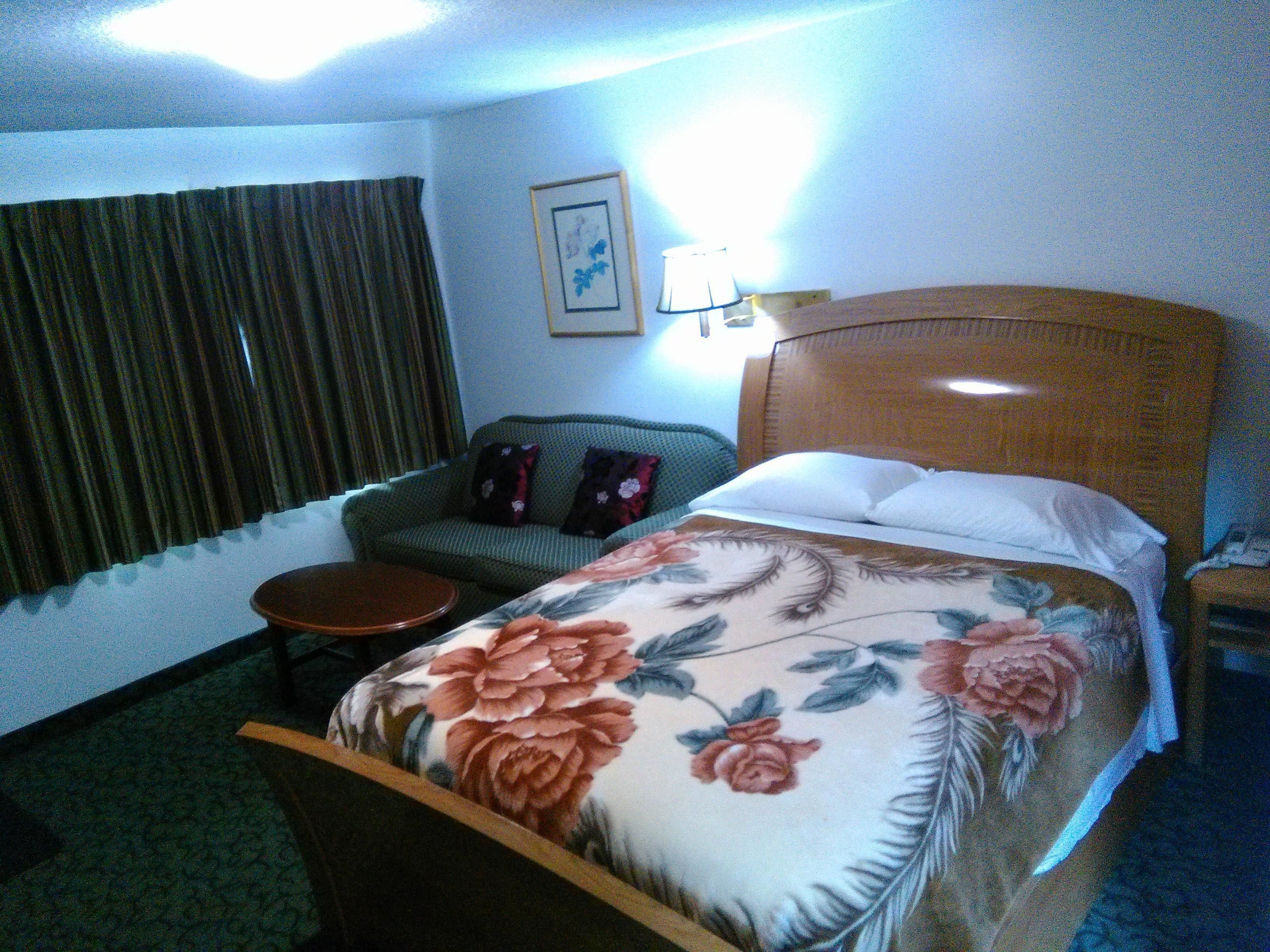 Una habitación de hotel con una cama, un sofá verde, una mesita redonda y una lámpara.