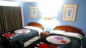 Habitación de hotel con dos camas, cada una con colcha estampada, mesita de noche, lámpara y cortina.