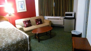 Habitación de hotel con cama, sofá, pequeña mesa, aire acondicionado y microondas.