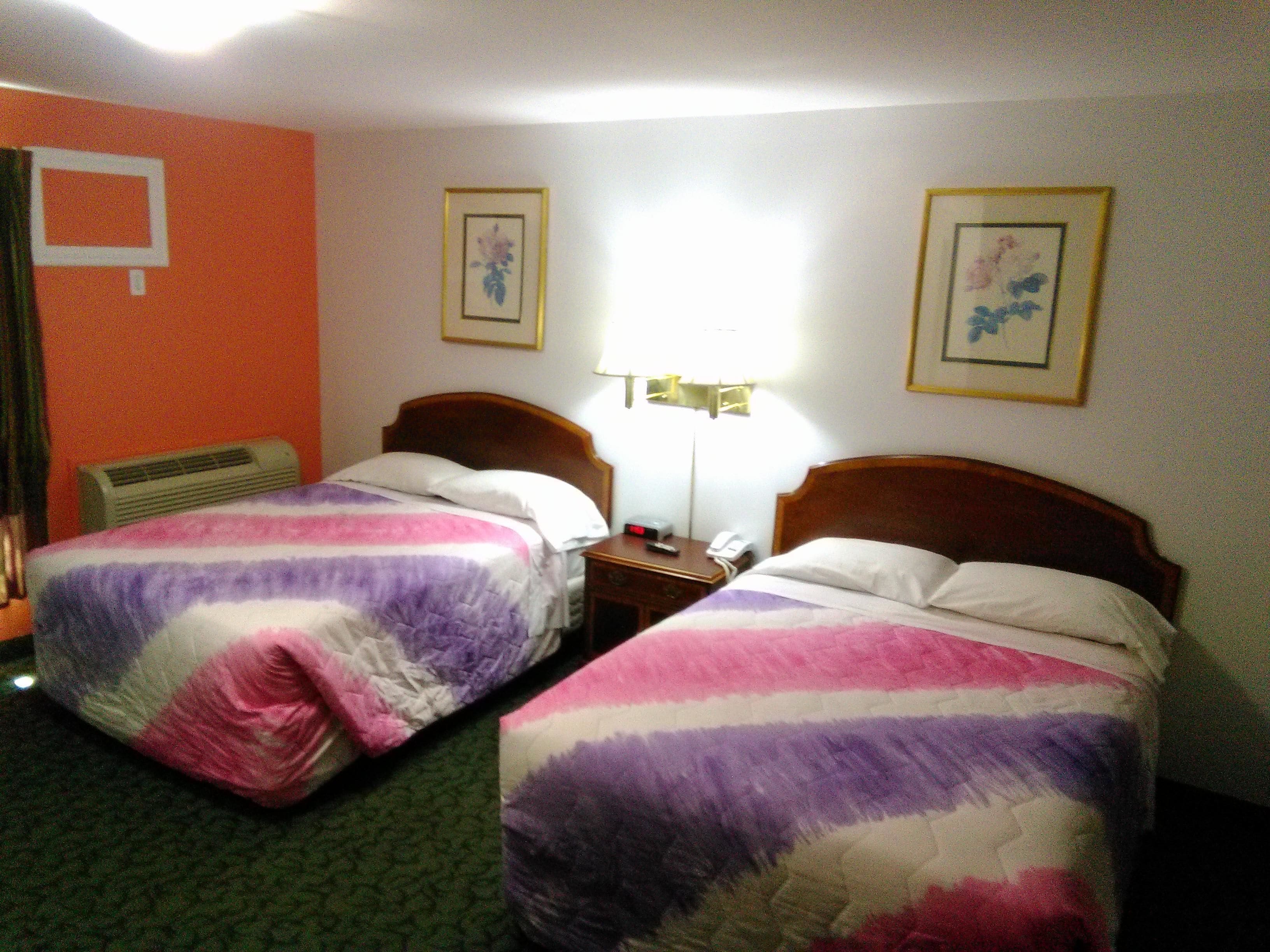 A hotel room with two single beds, a bedside table with a lamp, a telephone, and framed pictures on the walls.