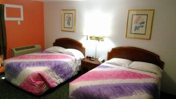 A hotel room with two single beds, a bedside table with a lamp, a telephone, and framed pictures on the walls.