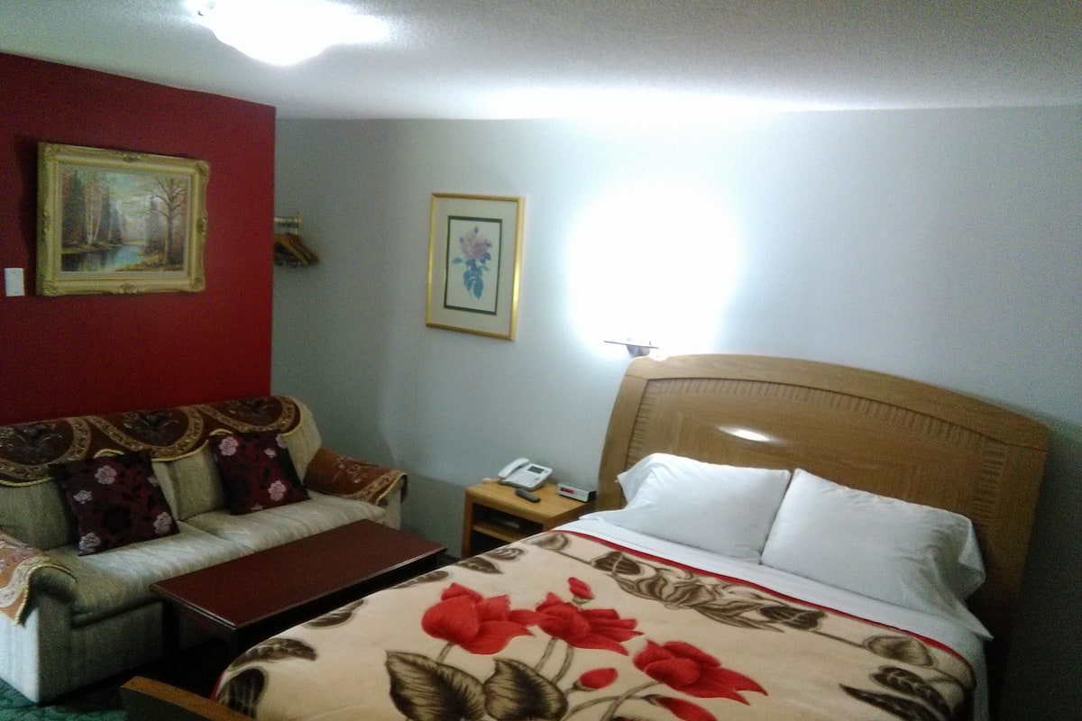 Una habitación de hotel con cama, sofá, mesita de noche y un cuadro en la pared.