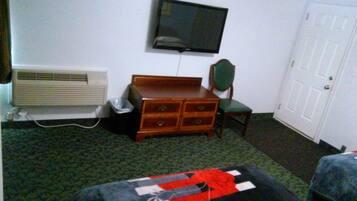 A hotel room with a bed, a dresser, a television mounted on the wall, a heater, and a door.