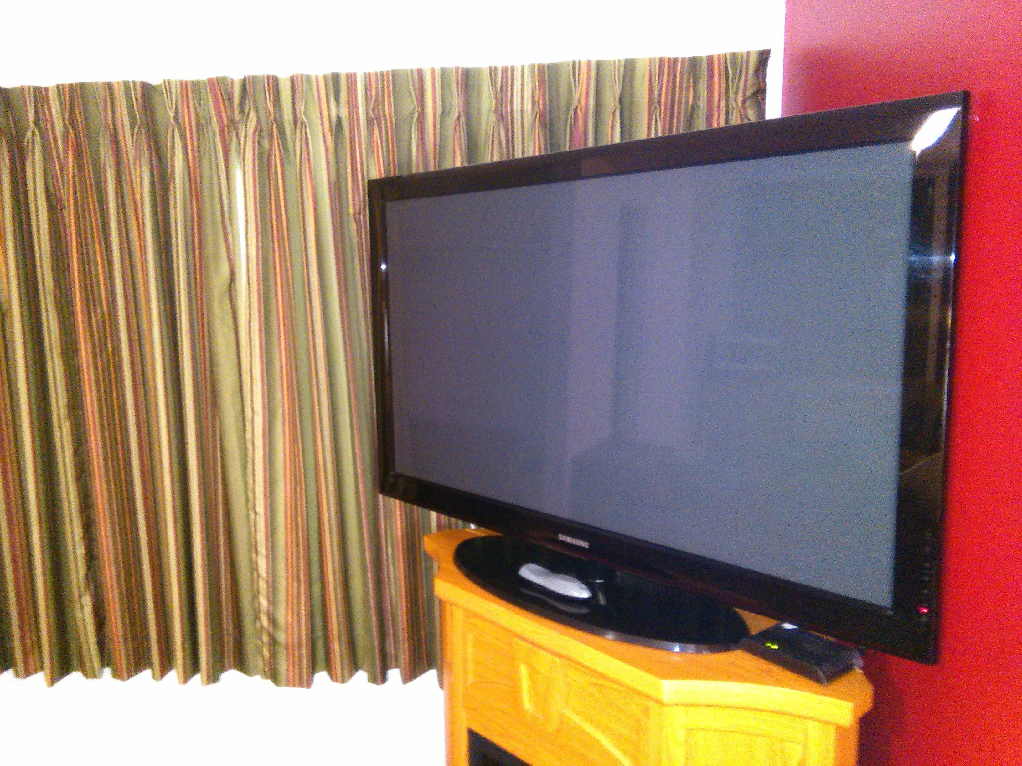 Un televisor de pantalla plana sobre un soporte de madera frente a una pared con cortina a rayas.