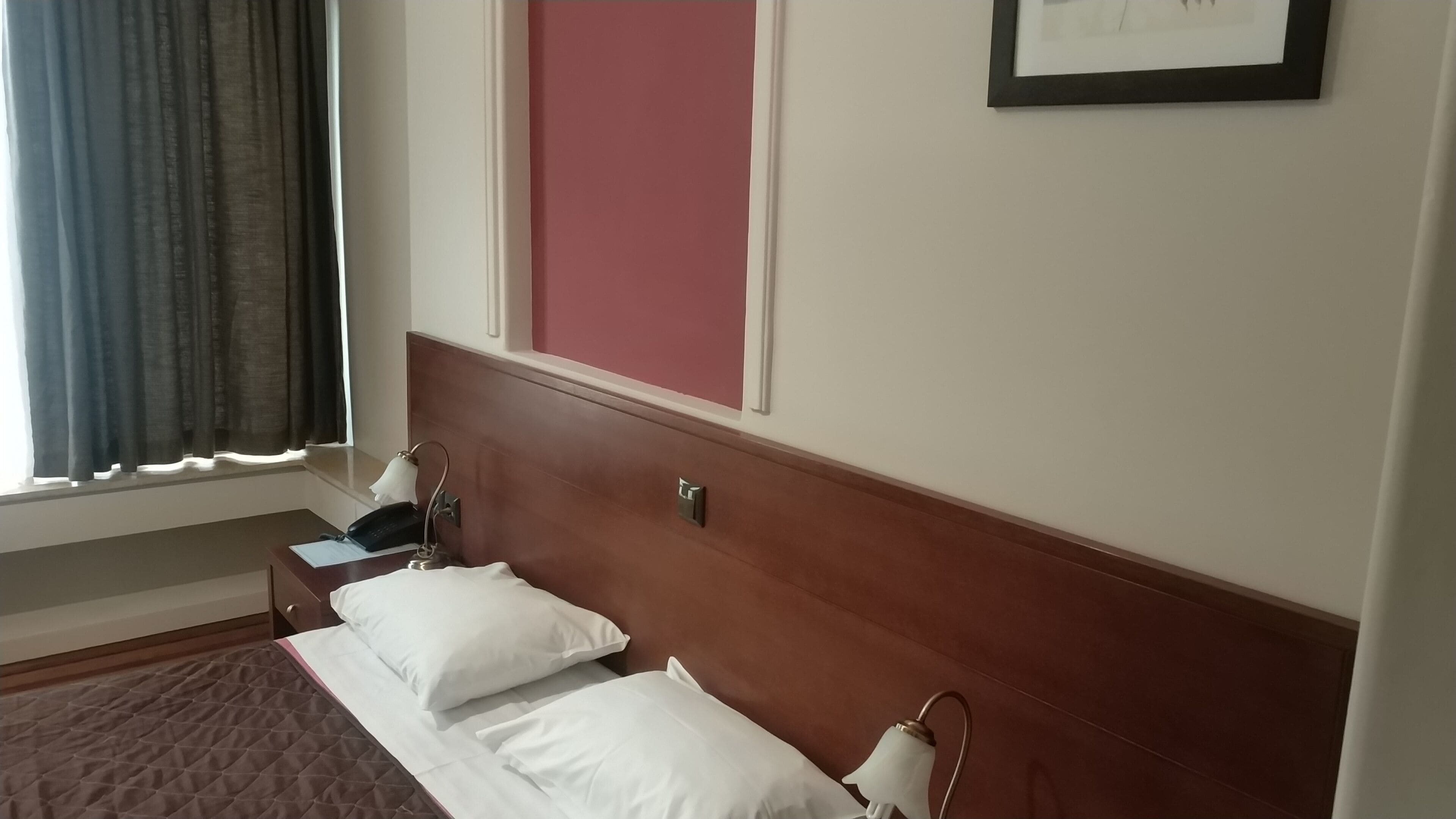 A hotel room with a bed, a bedside table, a telephone, and a framed picture on the wall.