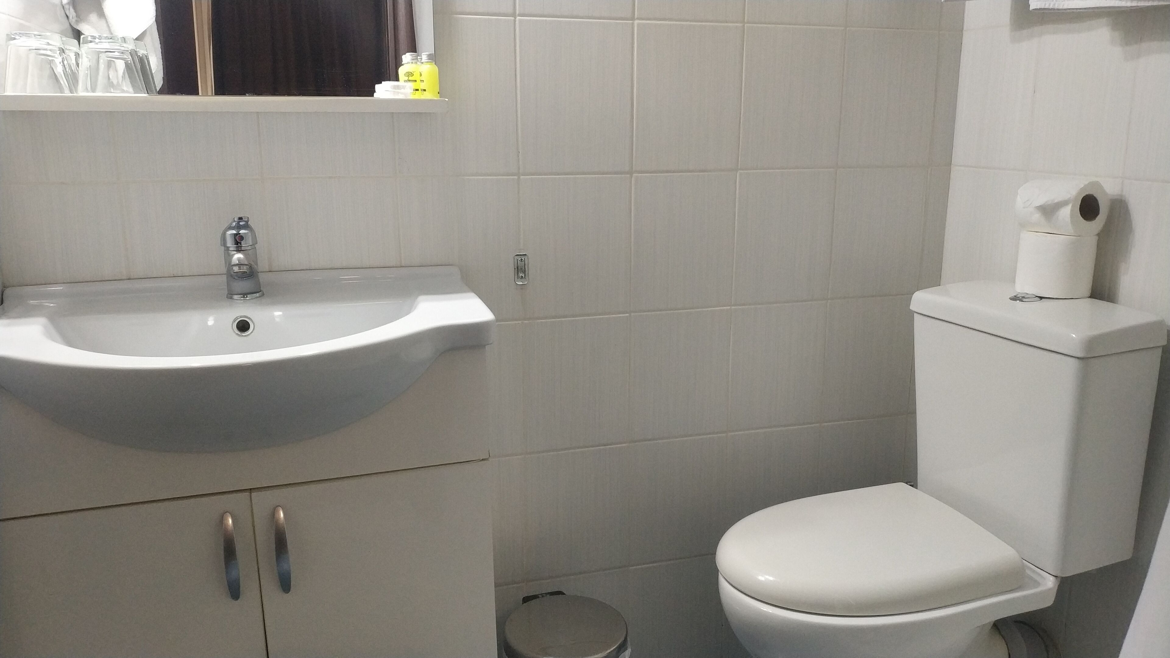 Casa de banho com lavatório branco, sanita e um pequeno contentor de lixo.