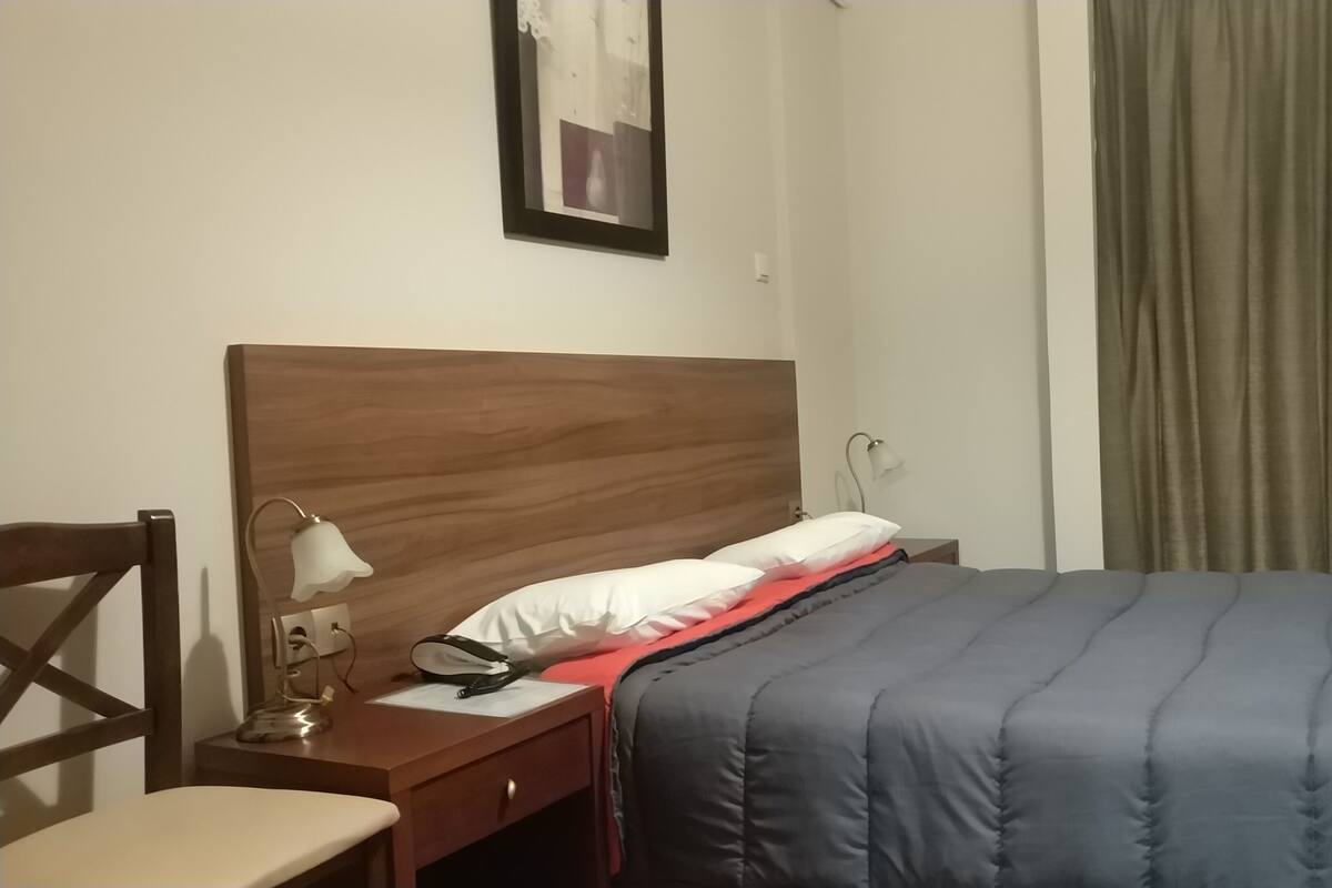 A hotel room with a wooden headboard, a bedside table with a lamp, a chair, and a bed with a blue blanket.