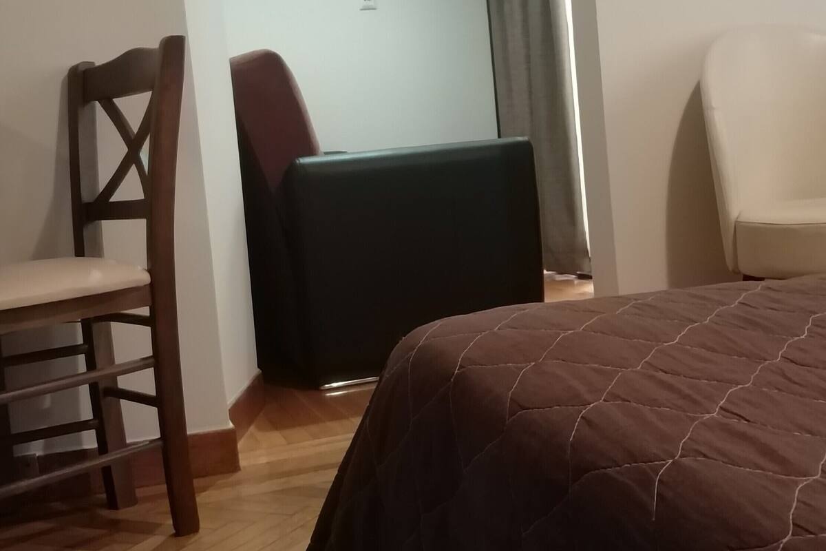 A hotel room with a bed, a TV, an air conditioner, a chair, and a desk.