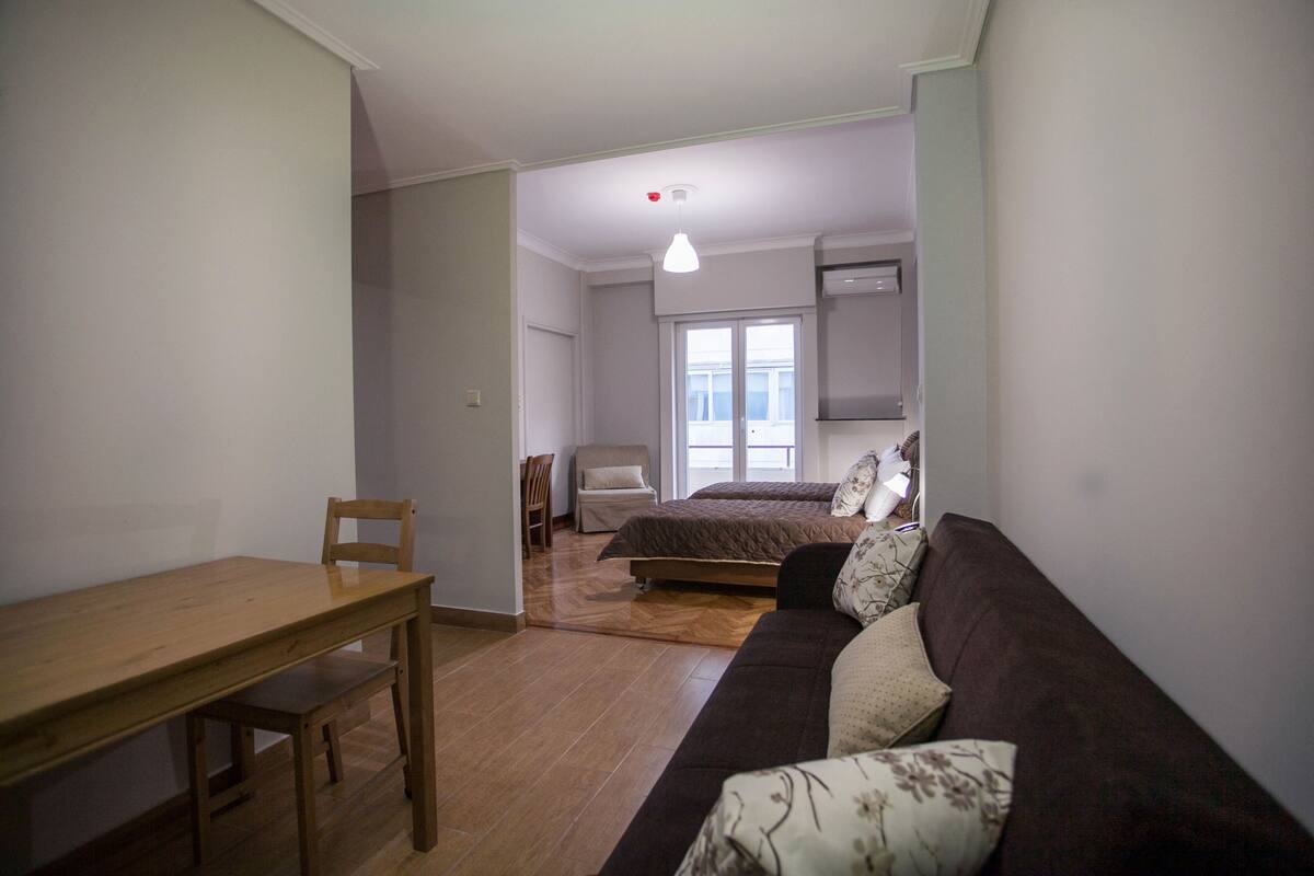 A compact living space with a wooden dining table, a sofa, a bed, and a chair.