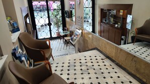 A hotel lobby with a check-in counter, seating area, and a view of the street outside. - Ambrosia Suites & Aparts (Athens)