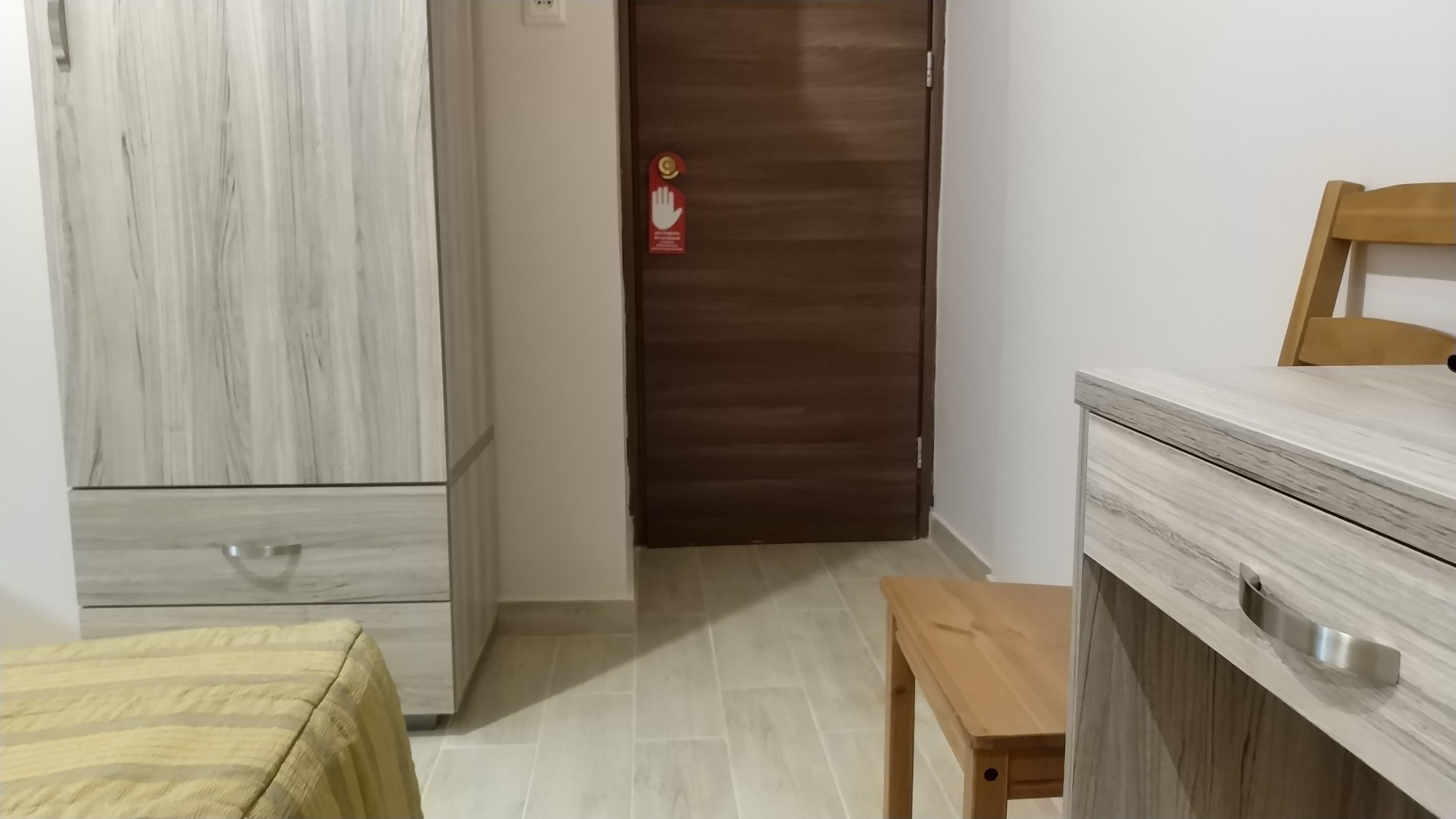 Una habitación con armario, cama, mesa de madera y puerta con cartel de seguridad.