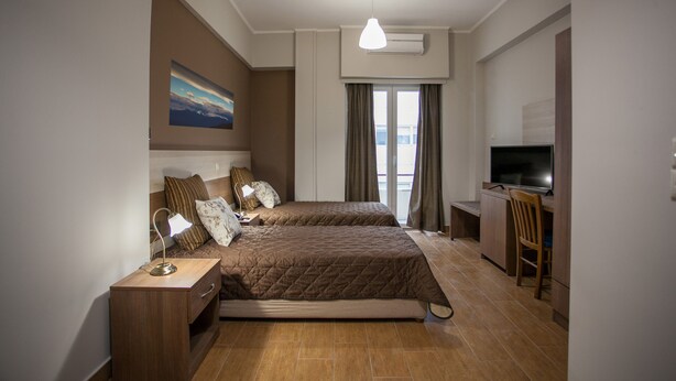 A modern hotel room with two beds, a desk, a TV, and a large window with curtains. - Ambrosia Suites & Aparts (Athens)