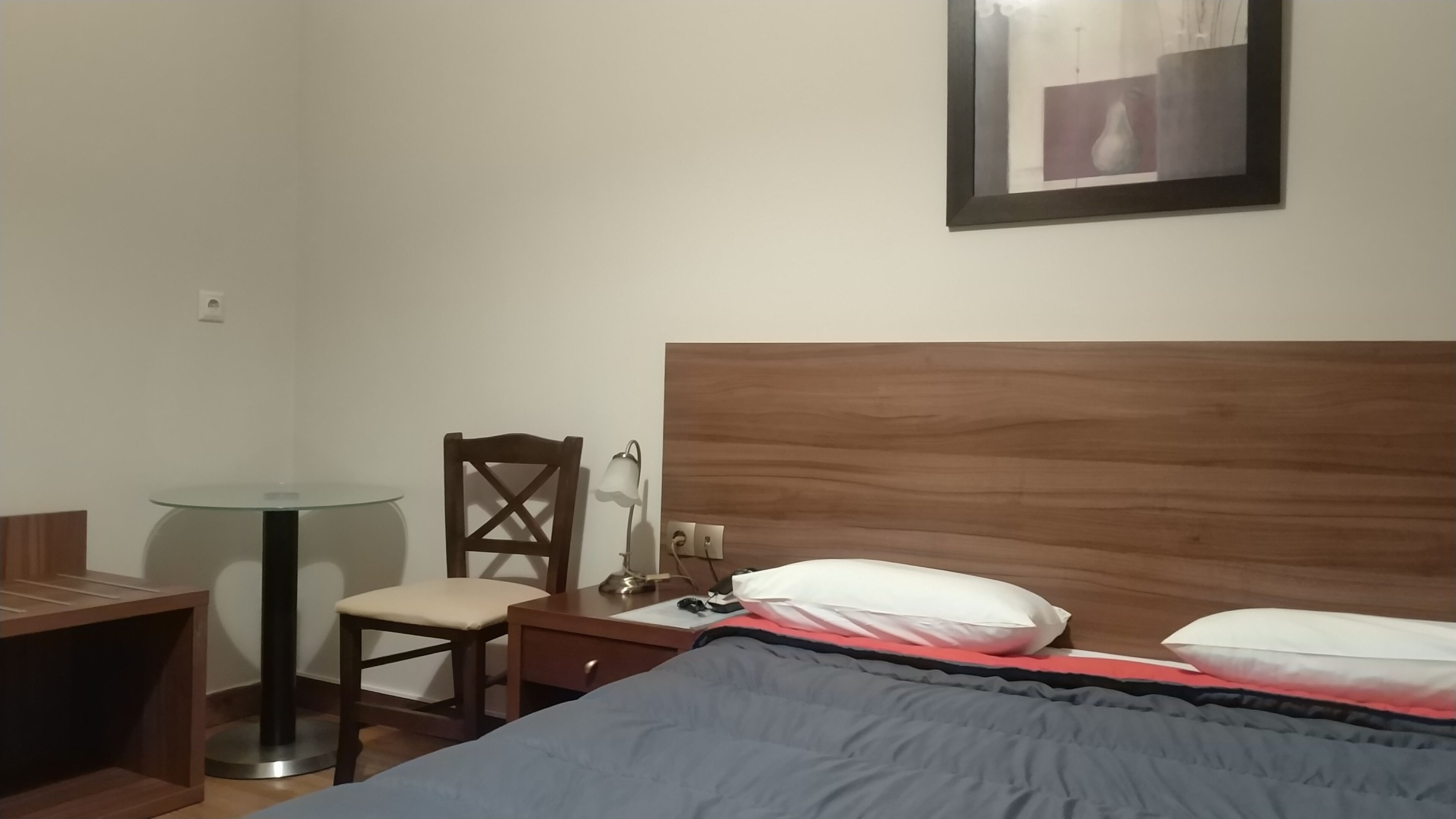 Une chambre d’hôtel avec un lit, un bureau, une chaise, une lampe et un tableau encadré au mur.