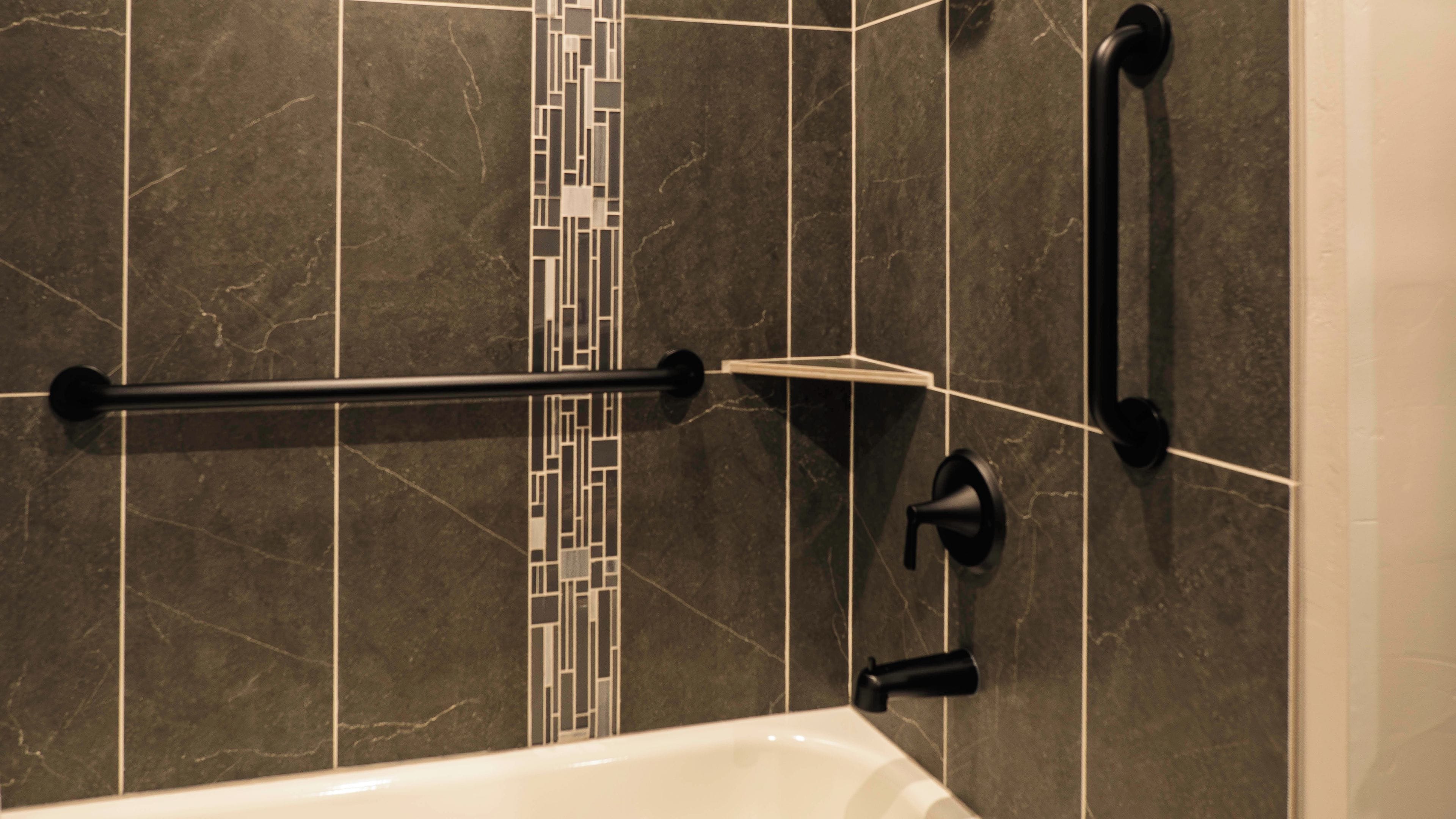 Un baño con bañera, barra de apoyo y pared con azulejos.