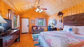 A cozy wooden cabin bedroom with a bed, a television, a sofa, and a ceiling fan.