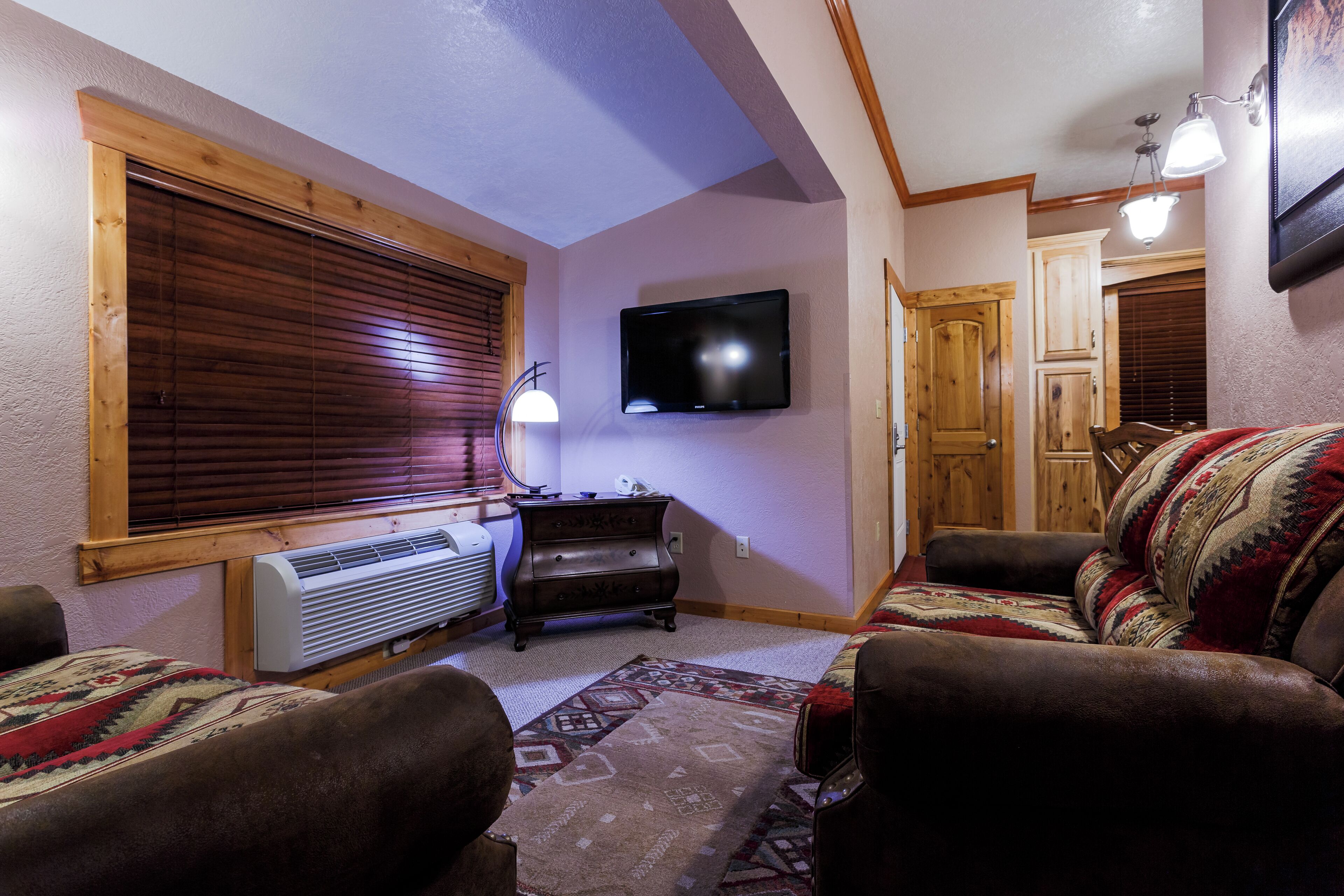 A living room with a fireplace, a television, and a large window with blinds.