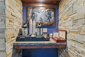 A stone wall with a hot water dispenser, a coffee maker, and a framed picture on a counter.
