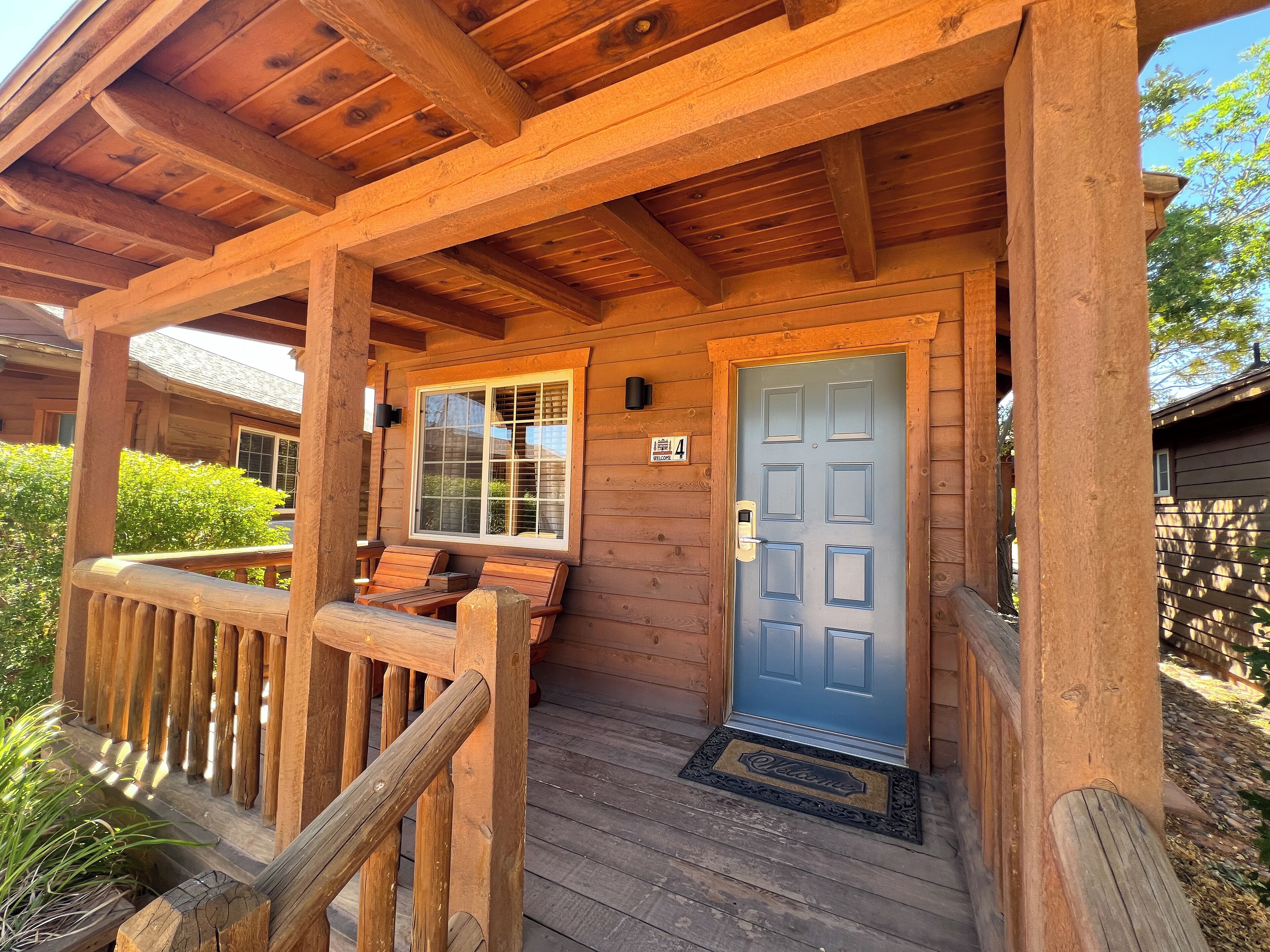 A wooden porch with a bench, a blue door, and a welcome mat.