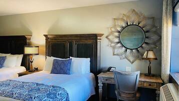 A hotel room with a large bed, a desk, a chair, a desk lamp, a telephone, and a decorative mirror.