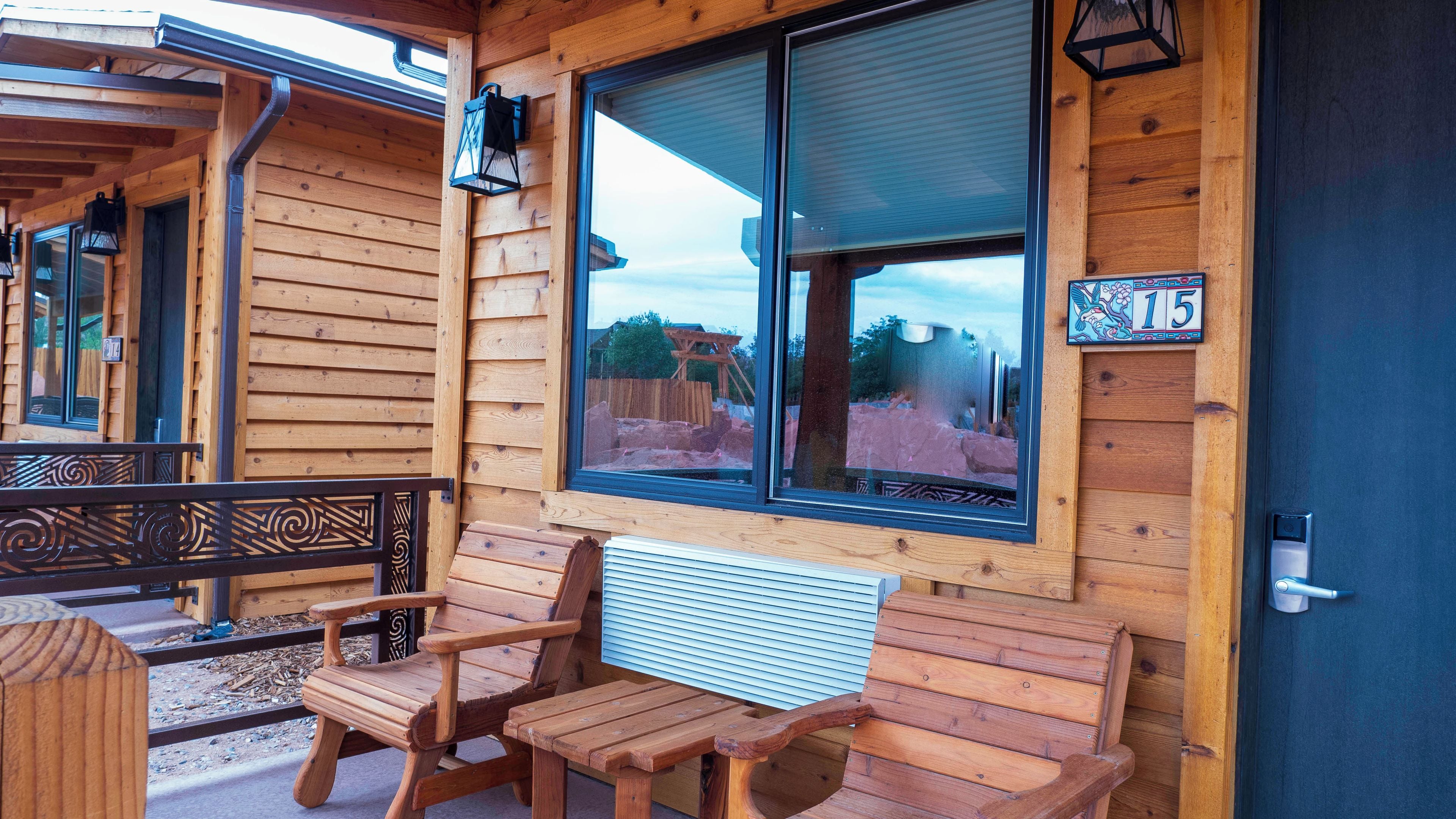 A wooden cabin with a porch, a bench, and a window with a view of a construction site.