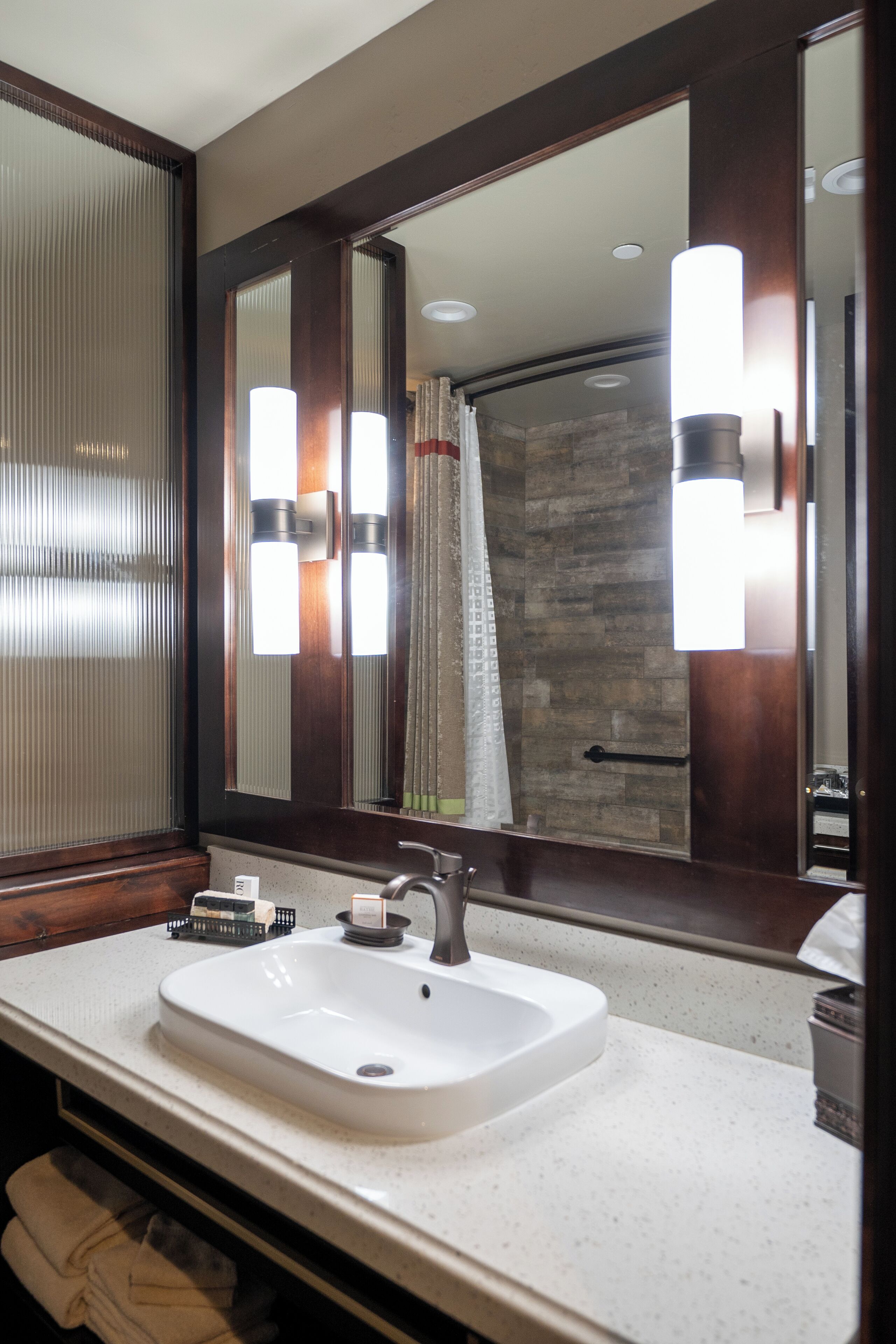 Une salle de bain avec un lavabo blanc, un grand miroir et un rideau de douche.