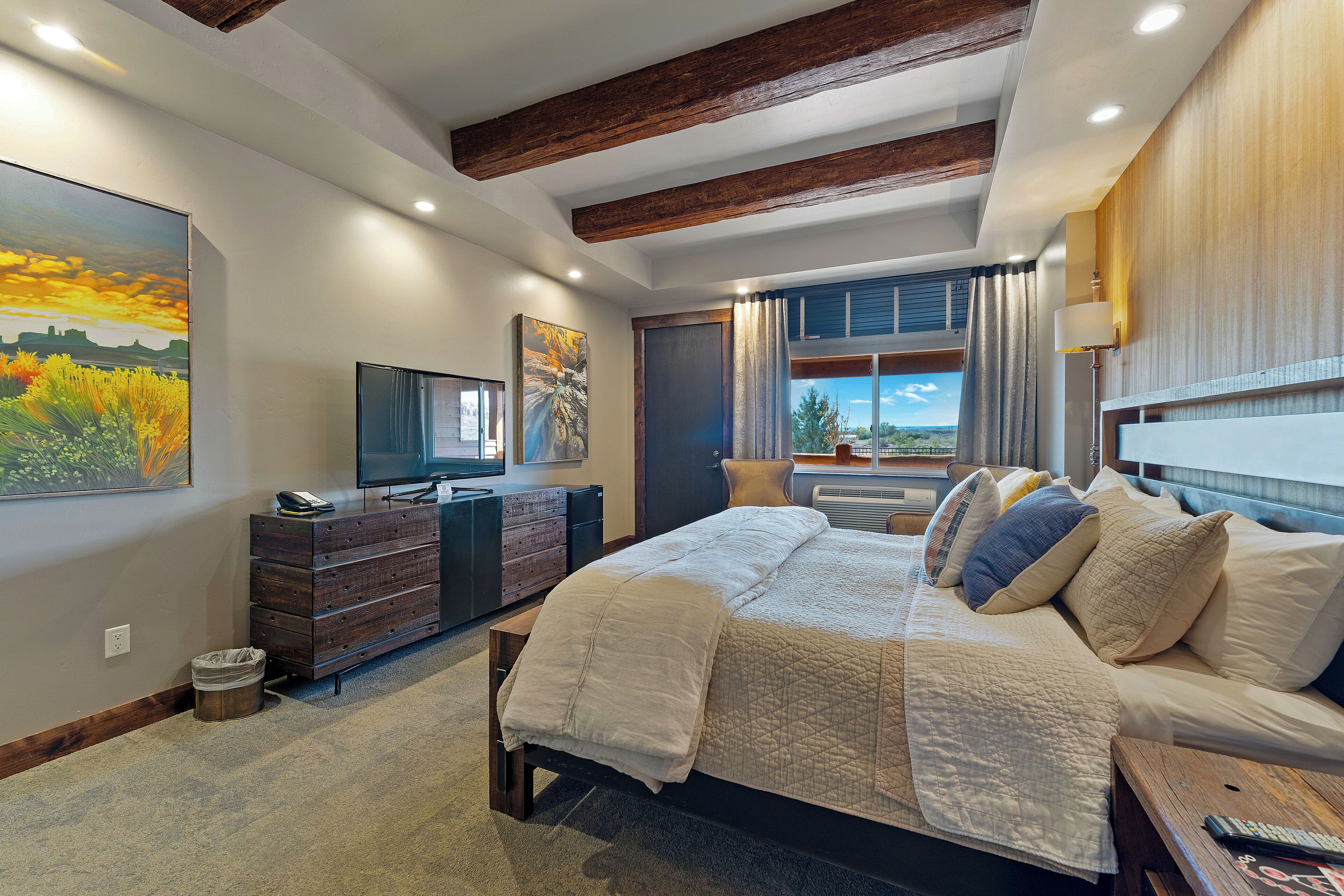 Une chambre à coucher avec un grand lit, une télévision, une commode et une fenêtre donnant sur un beau paysage.