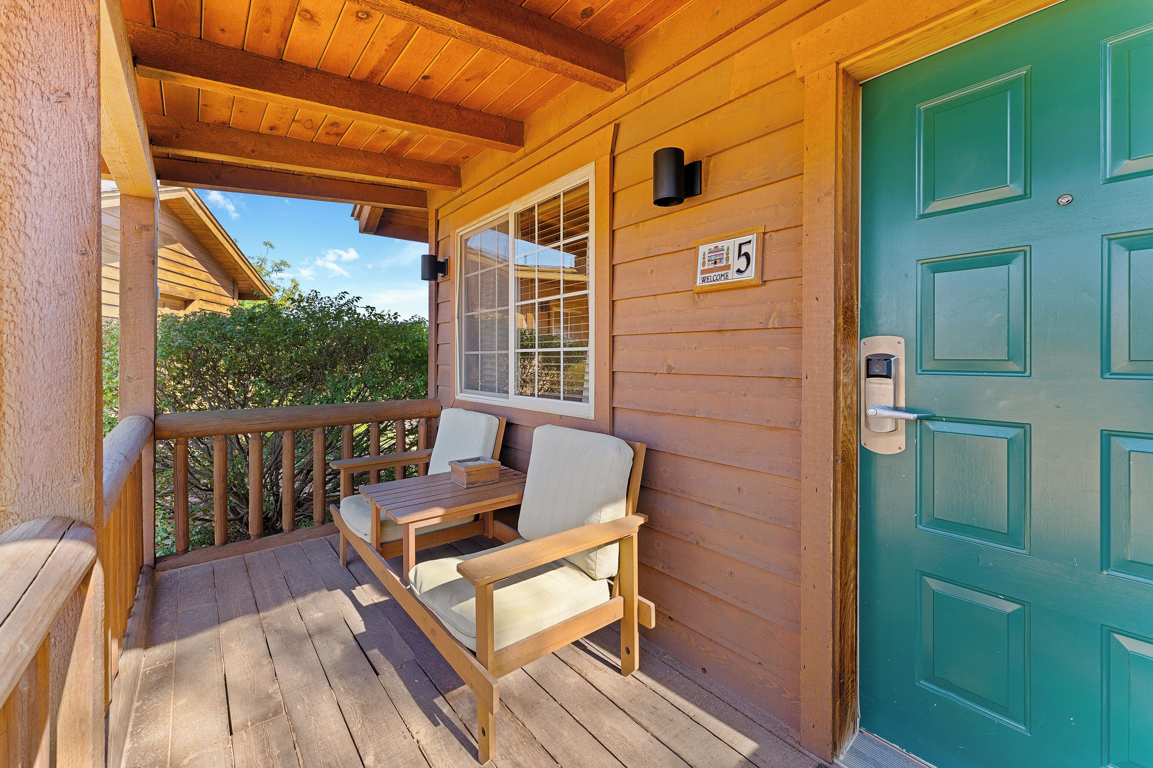 A wooden deck with a table and chairs, a green door, and a welcome sign.