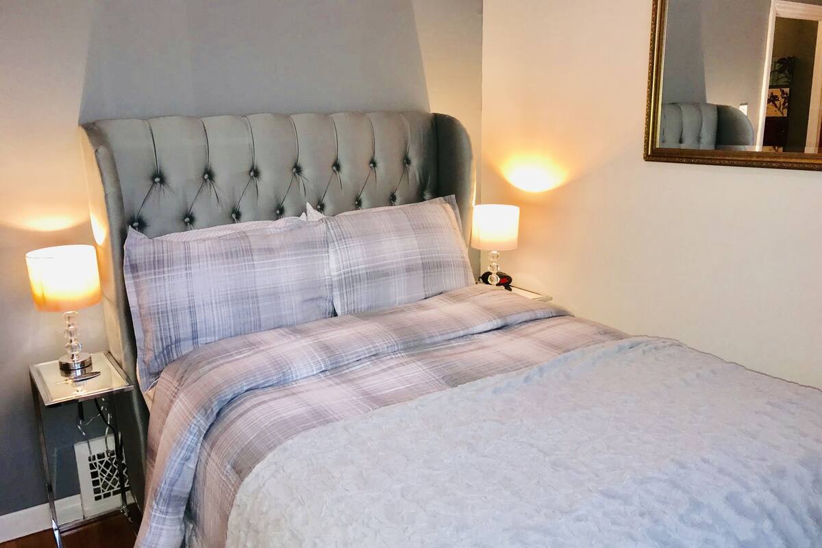 Een netjes opgemaakt bed met een gestapeld hoofdbord, twee nachtkastjes met lampen en een spiegel aan de muur.