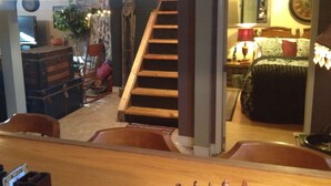 Une pièce avec un escalier en bois, un lit recouvert d’une couverture verte, une commode en bois et une chaise.